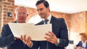 Two men in formal suits review a document together inside a brick-walled office, conveying a collaborative and professional atmosphere.